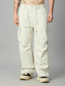 A person wearing very loose off-white cargo pants with a drawstring waist and large side pockets, paired with cream sneakers, photographed against a plain light gray studio background.