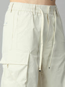 Close-up of a person wearing off-white cargo pants with an elastic drawstring waist, side pockets, and a large front cargo pocket, photographed against a light gray studio background.