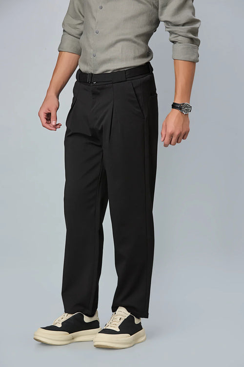 Person wearing black pleated pants with a gray shirt on a light gray background