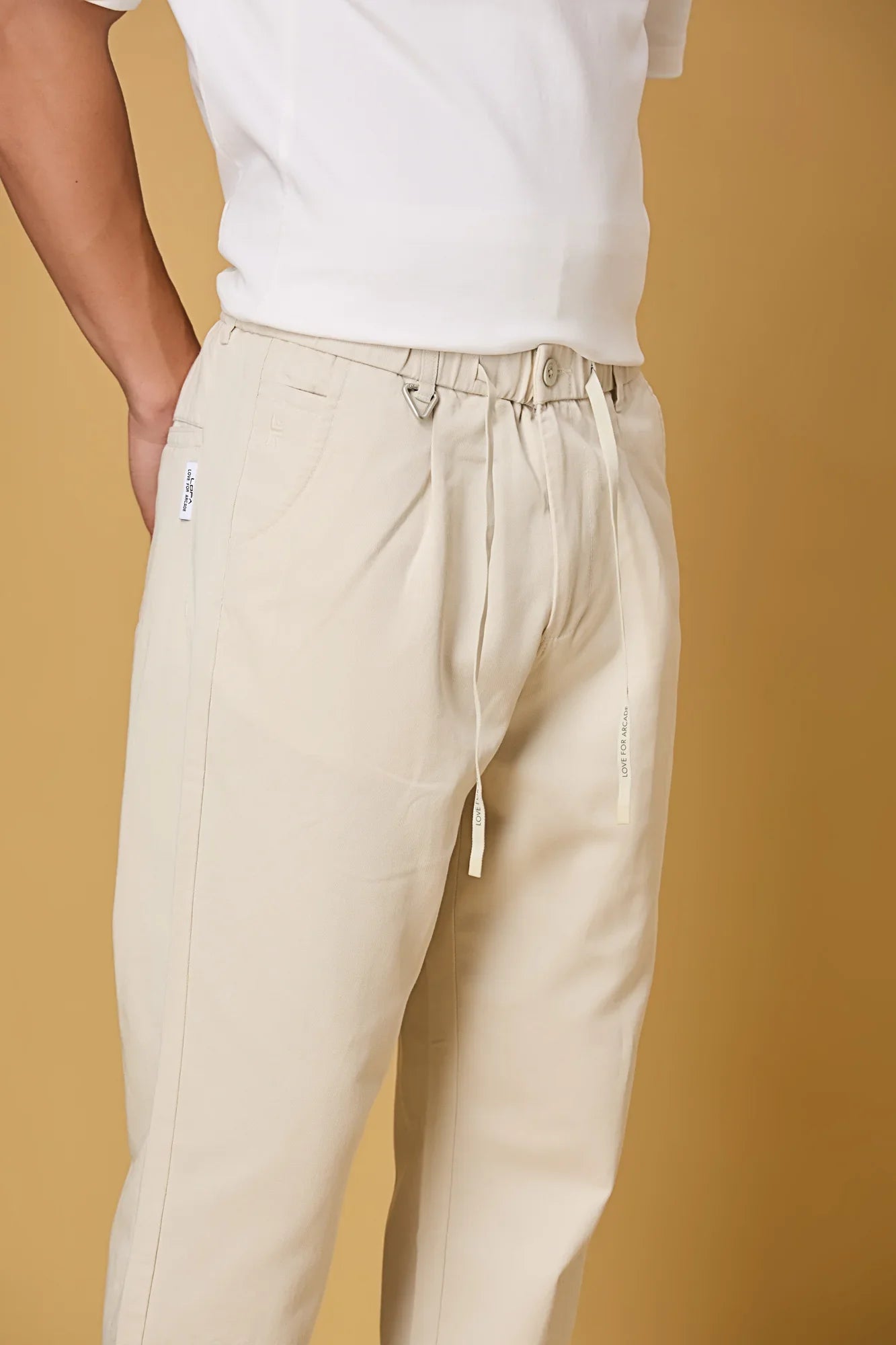 Close-up of beige trousers waist string, triangle ring, and fabric texture.
