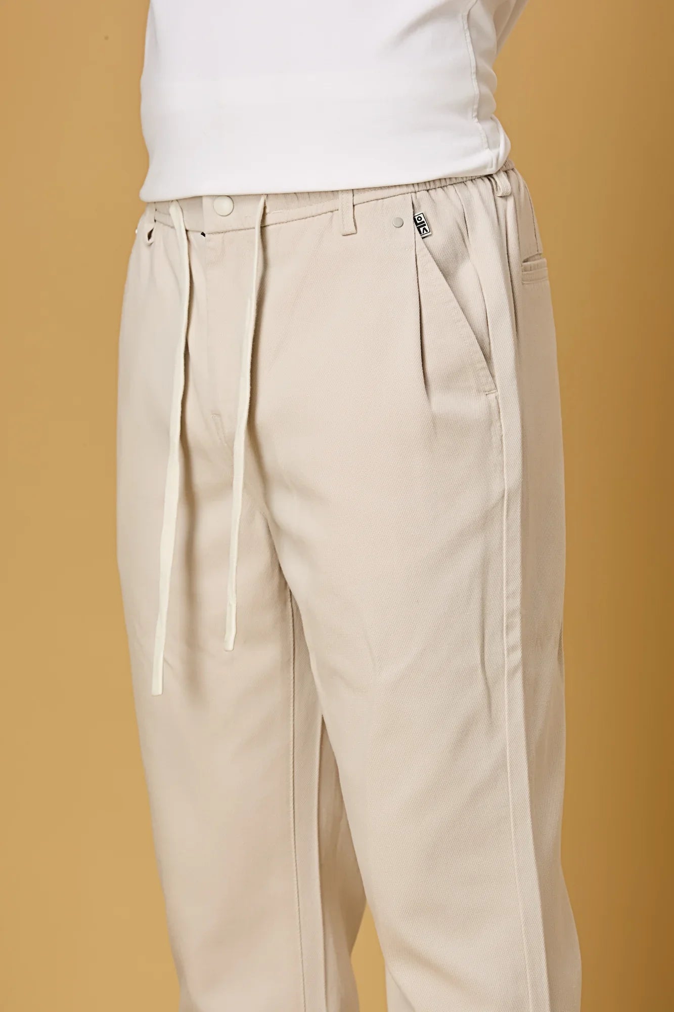Close-up of waist string, press button, and fabric texture on beige trousers.