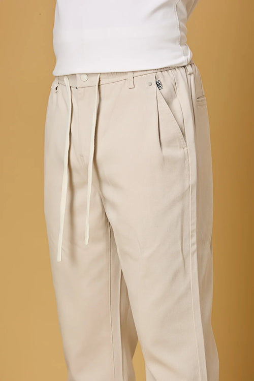 Close-up of waist string, press button, and fabric texture on beige trousers.