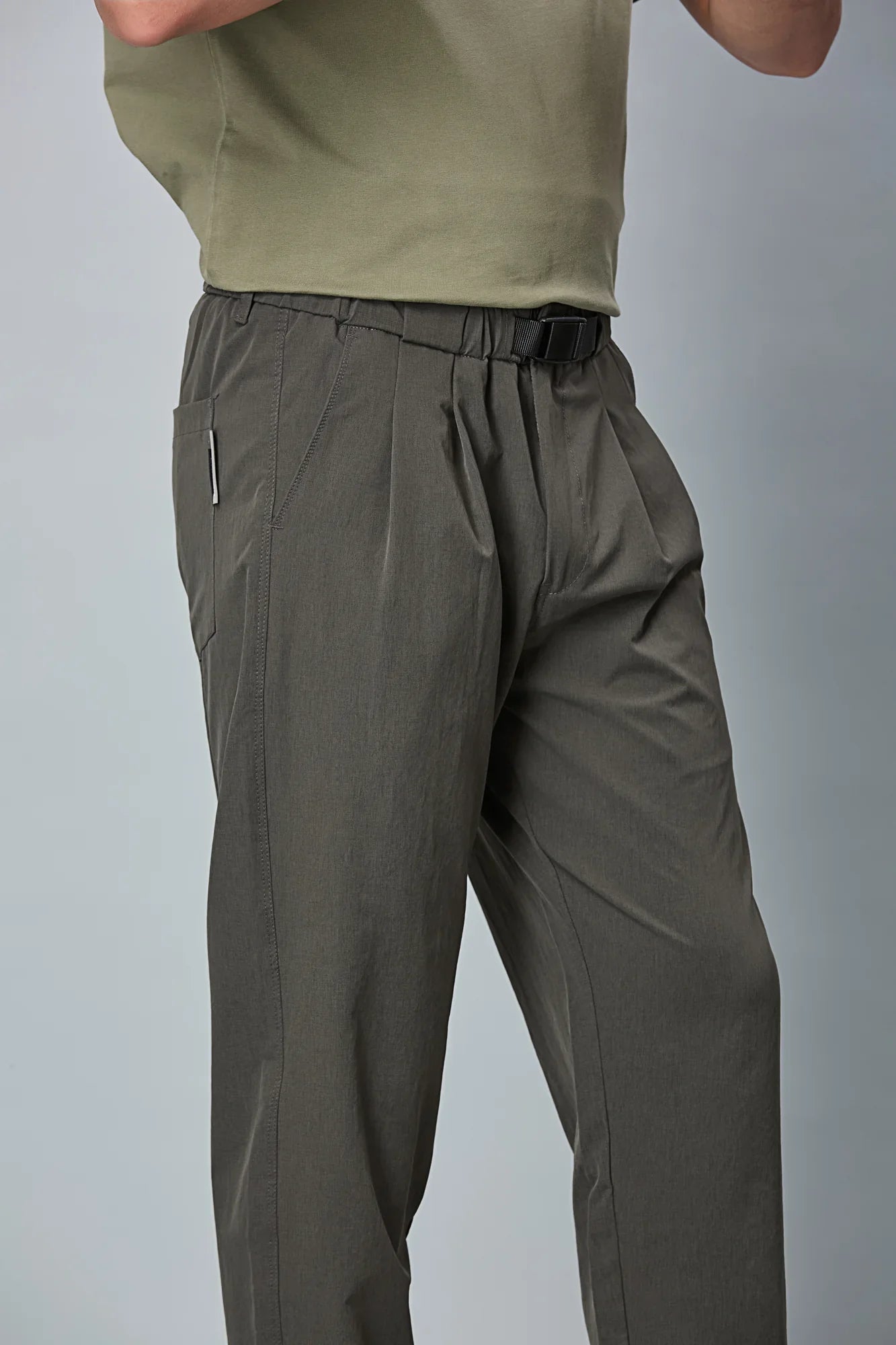 Close-up of grey trousers belt, elastic waist, and pleated design details