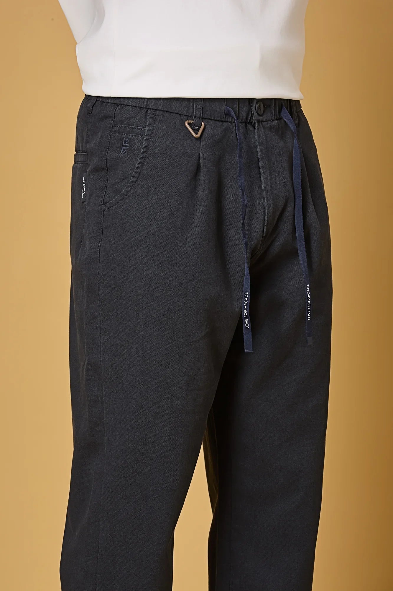 Close-up of navy blue trousers waist string, triangle ring, and fabric texture.