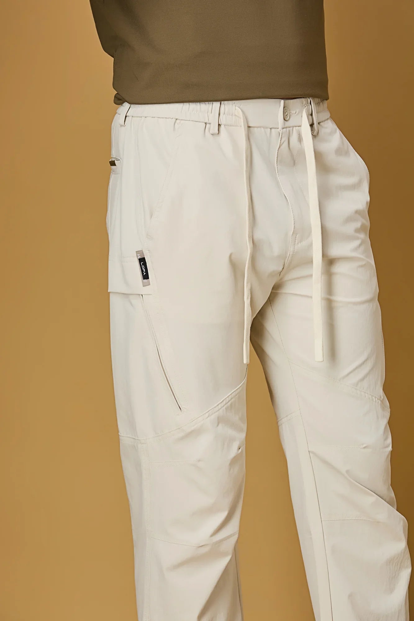 Close-up of beige trousers waist strings, side pockets, and smooth fabric texture.